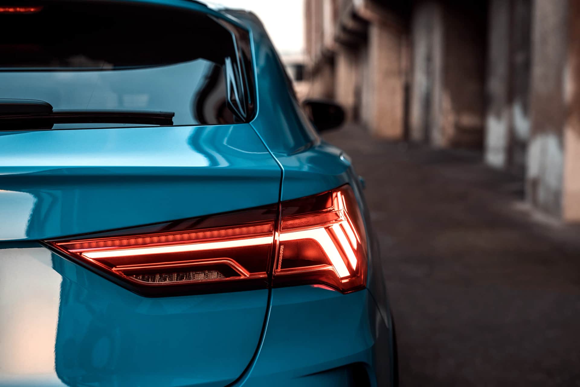 Detailaufnahme des Rueckleuchten-Lichtbands eines tuerkisblauen Audi Q3 vor Industriekulisse, Automotive-Shooting im warmen Abendlicht
