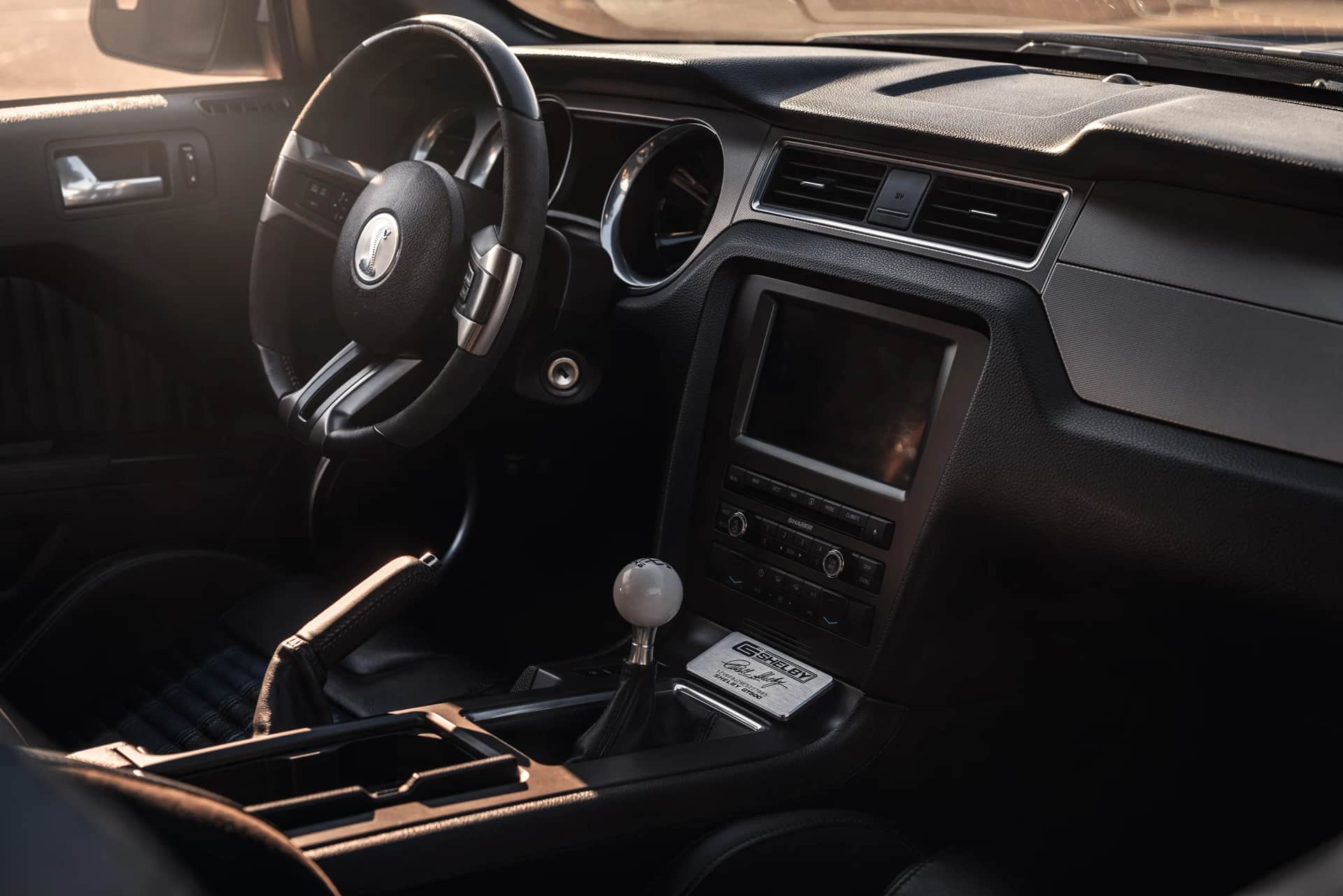 Cockpit des Ford Shelby Mustang mit Lederlenkrad, Schaltknauf und Cobra-Logo, warmes Lichtspiel beim Automotive-Interieur-Shooting