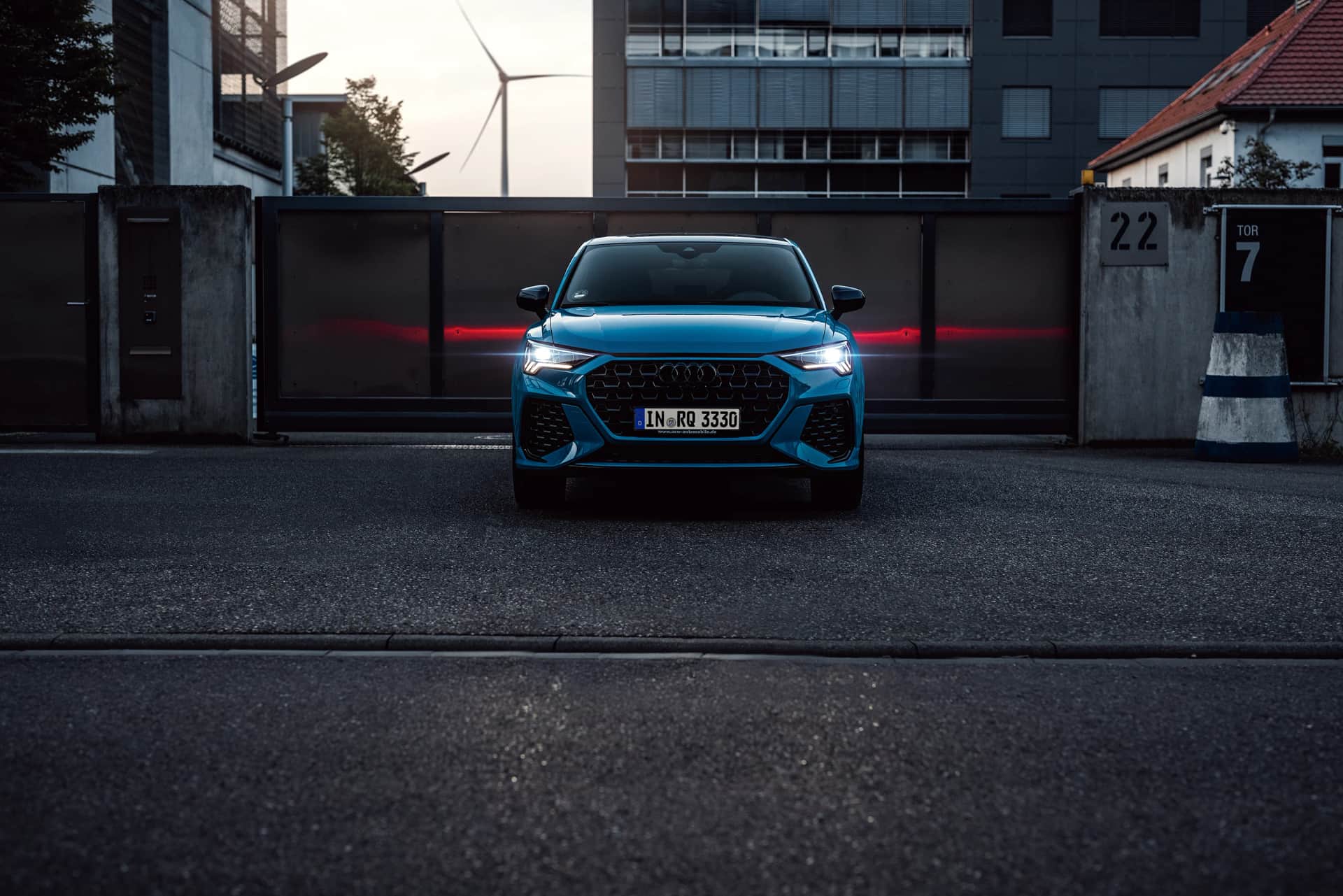 Blauer Audi Q3 Sportback frontal vor industrieller Toranlage mit Windrad, rote Lichtspur im Hintergrund beim Automotive-Shooting in Stuttgart