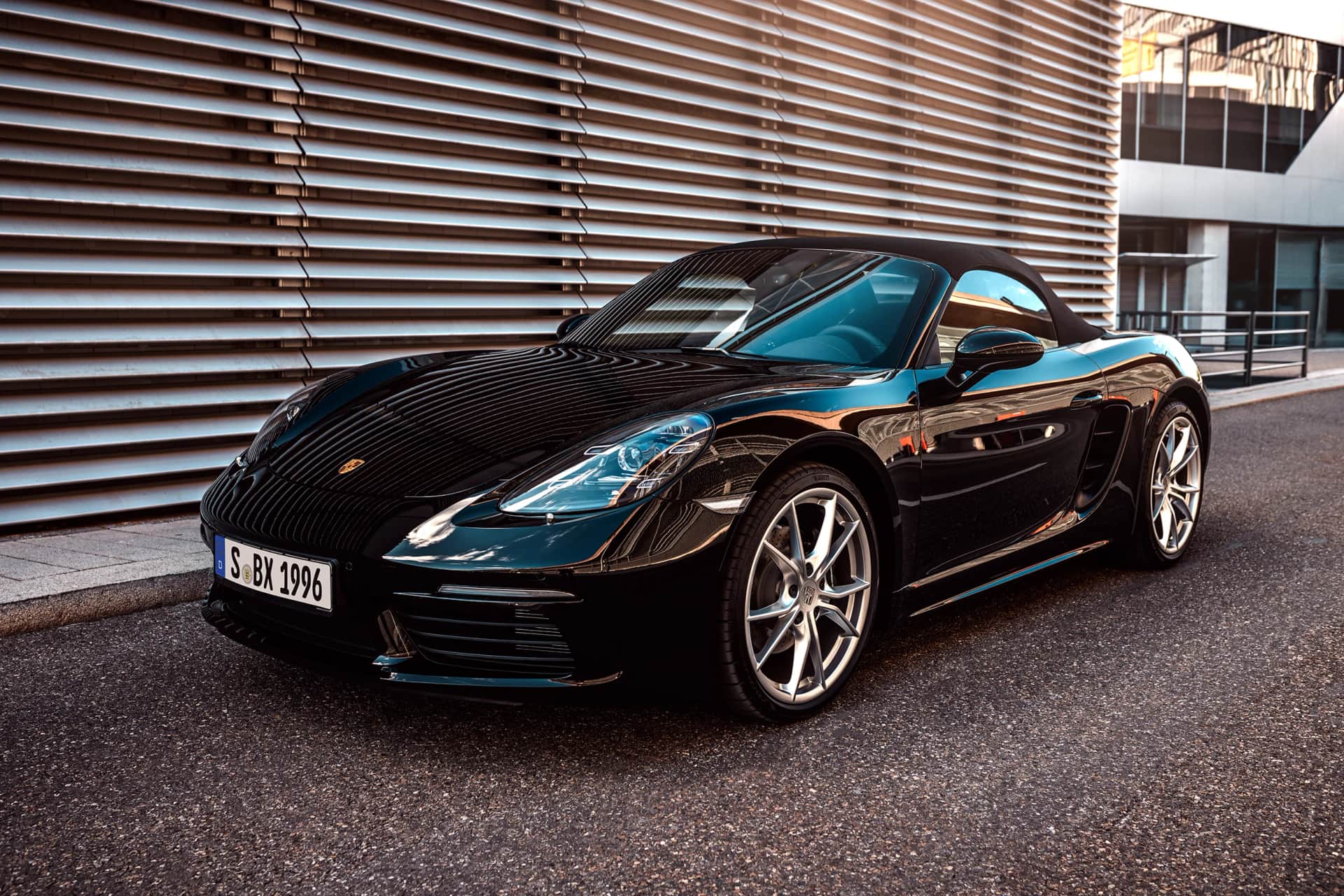 Schwarzer Porsche 718 Boxster in der Frontansicht vor einer geriffelten Metallfassade, warmes Abendlicht beim Automotive-Shooting in Stuttgart