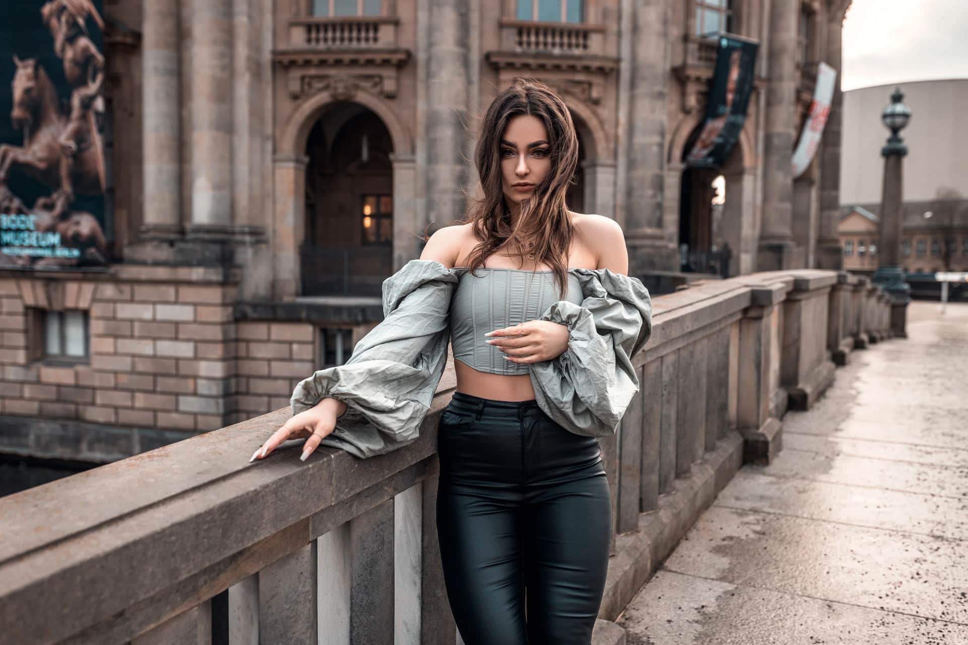 Frau mit langen Haaren in grauem Off-Shoulder-Top an einer Bruecke vor dem Berliner Bode-Museum, stimmungsvolles Editorial-Shooting in der Abenddaemmerung