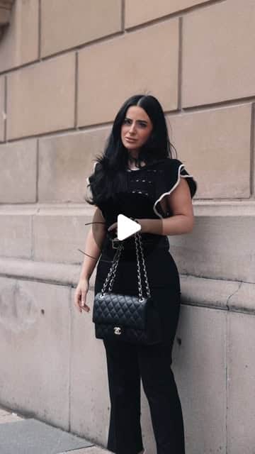 Frau in schwarzem Outfit mit gesteppter Designer-Handtasche an heller Sandsteinfassade, urbanes Fashion-Editorial