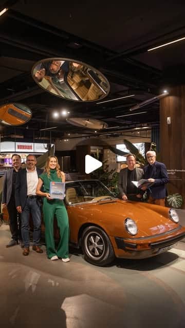 Gruppe von fünf Personen neben orangefarbenem klassischem Porsche 911 im modernen Showroom, Event-Aufnahme