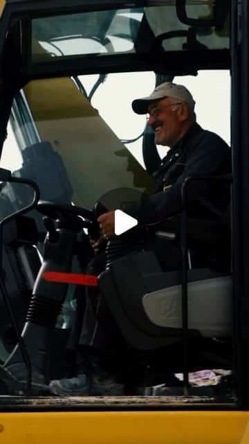 Lächelnder Baggerfahrer mit Cap in der Kabine eines Baufahrzeugs auf der Baustelle