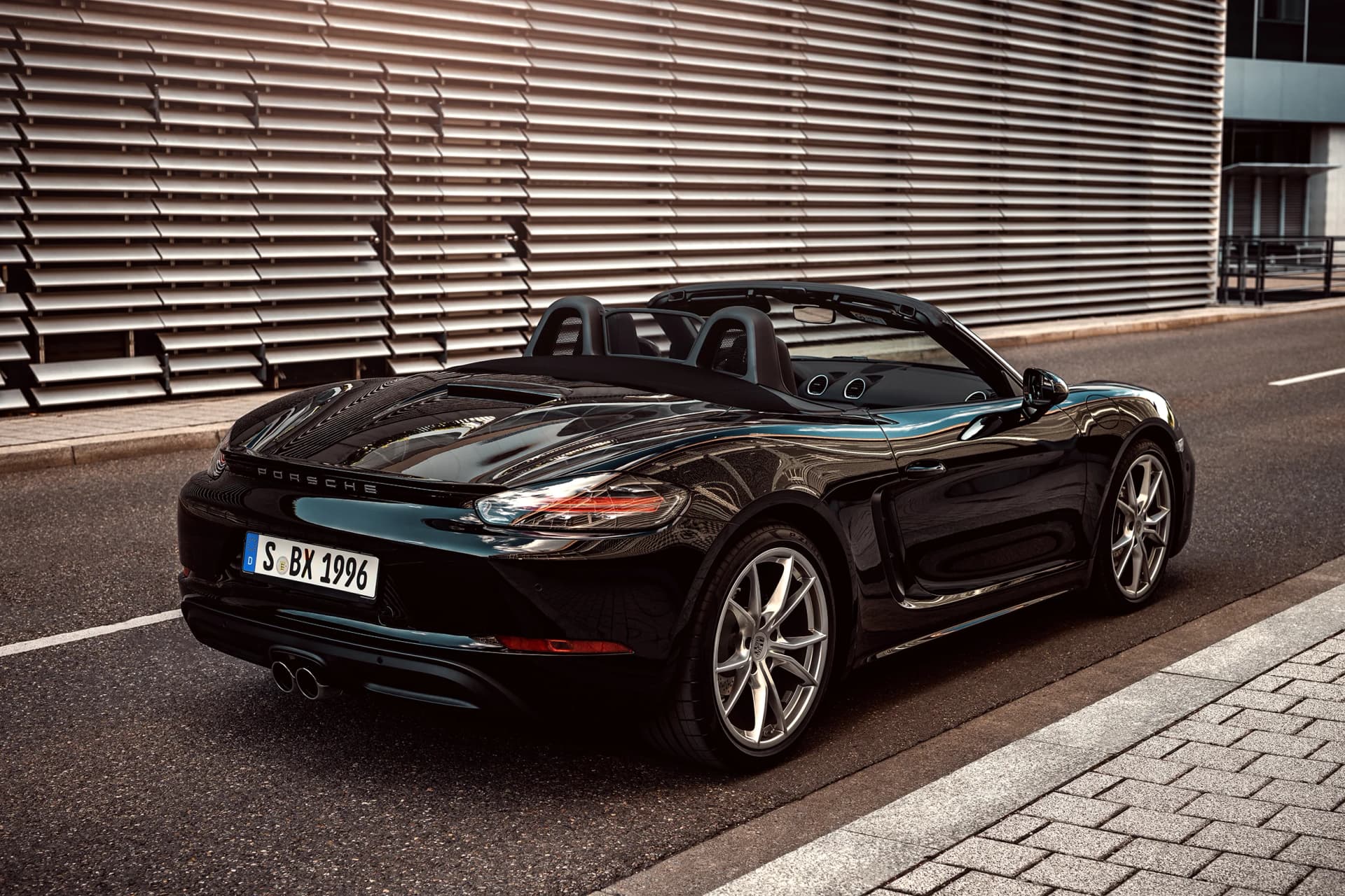 Schwarzer Porsche 718 Boxster Cabrio von hinten vor moderner Metallfassade am Strassenrand, elegantes Automotive-Shooting