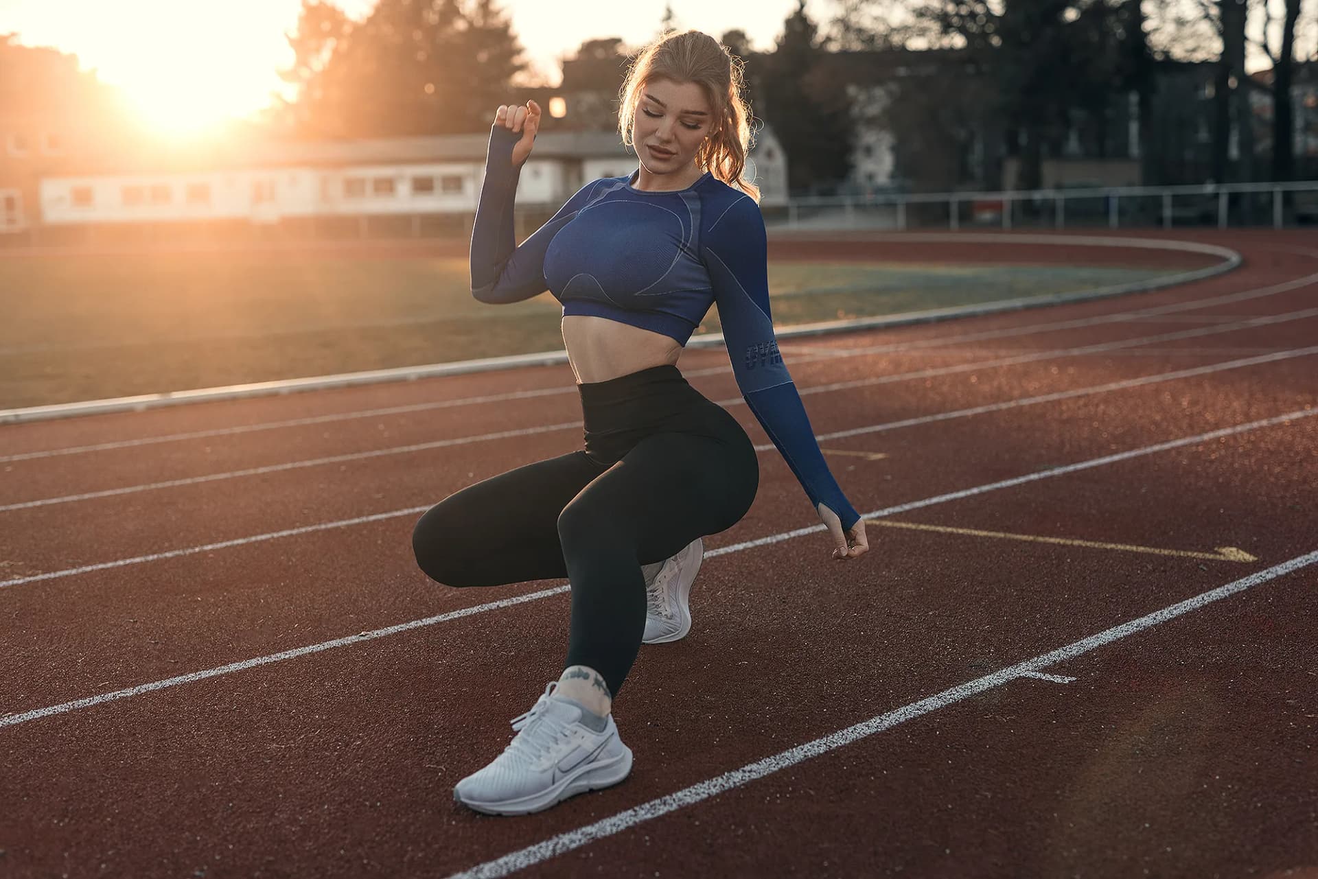 Sportlerin in der Startposition auf einer Laufbahn im goldenen Gegenlicht, dynamisches Fitness-Porträt