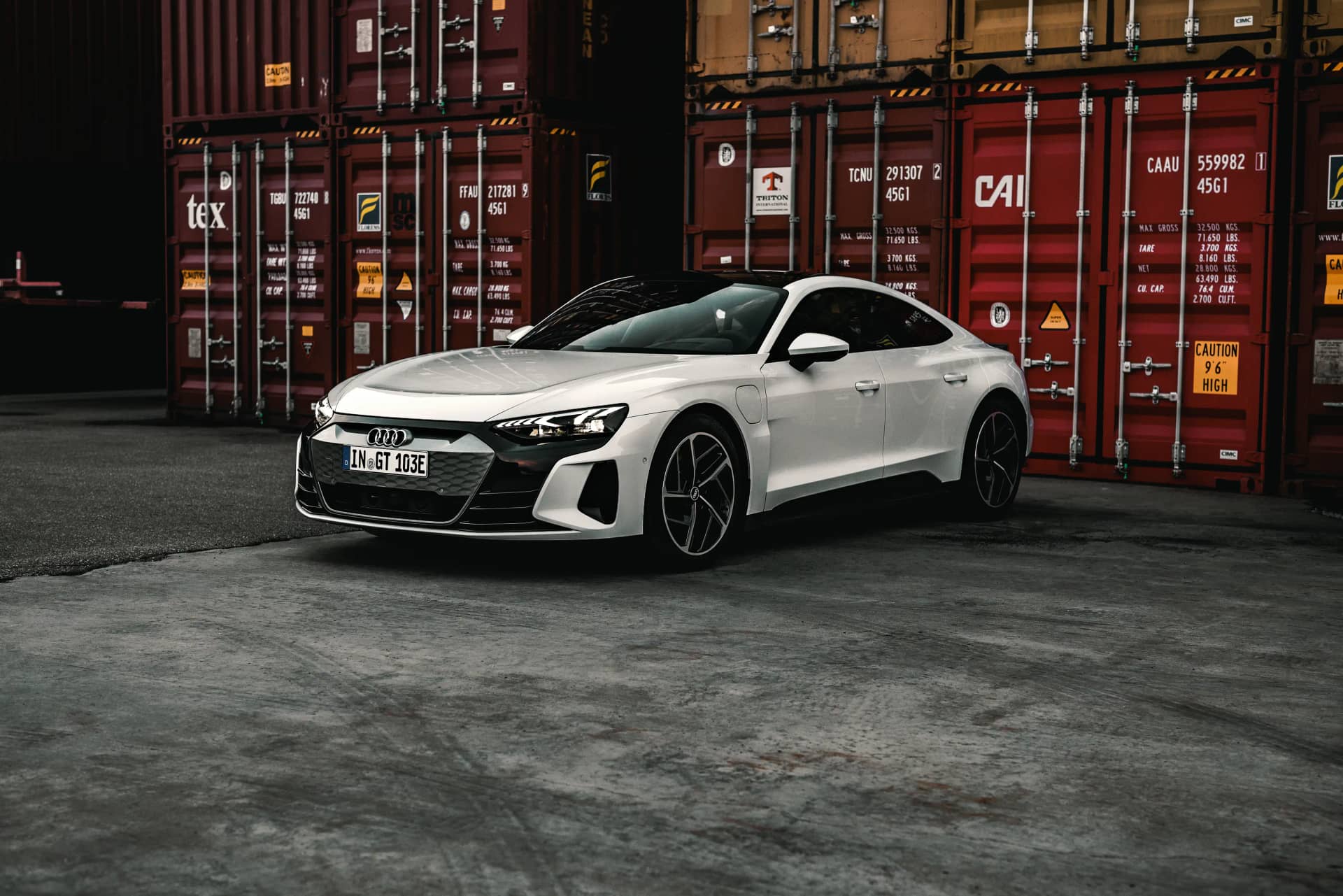 Weisser Audi e-tron GT in Frontansicht vor rotem Container-Stapel im Hafen, kontrastreiches Automotive-Shooting