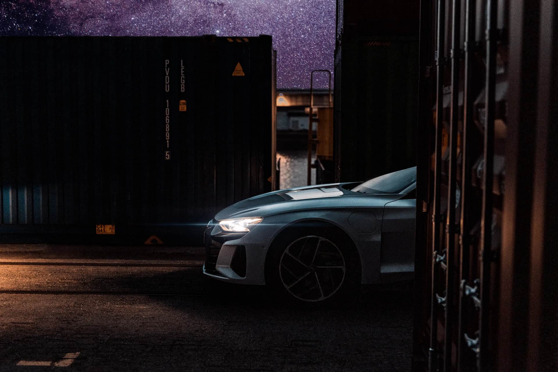 Sportliche Limousine zwischen Frachtcontainern unter Sternenhimmel, cineastische Automotive-Aufnahme bei Nacht