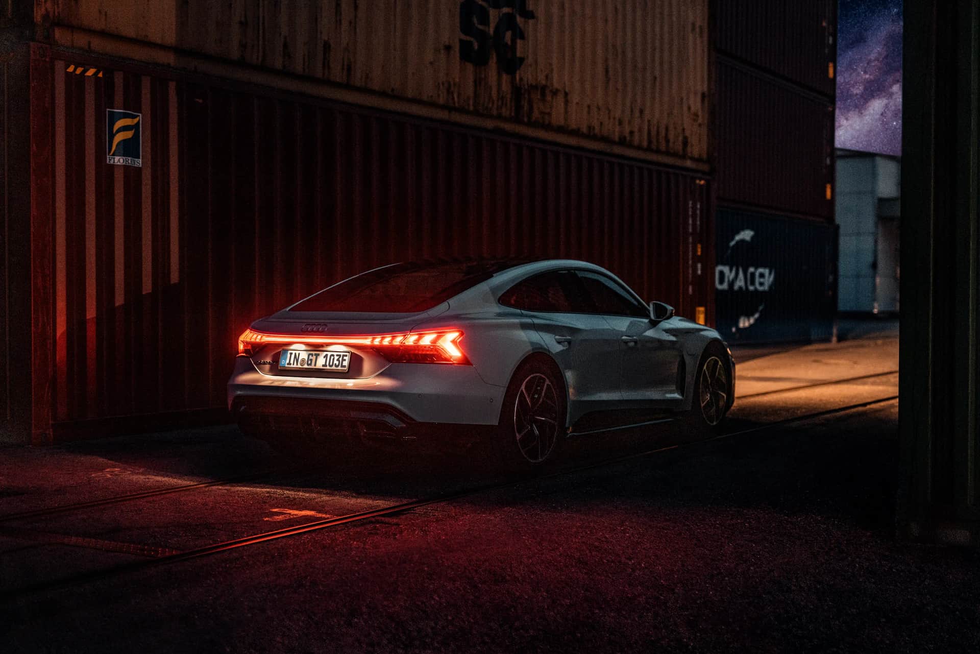 Heck eines weißen Audi e-tron GT mit roter Lichtsignatur in nächtlicher Container-Kulisse, Automotive-Aufnahme